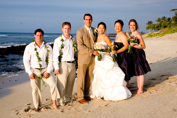 wedding party group portrait beachside - bride in white ball gown, bridesmaids in dark purple short bridesmaids dresses - real wedding photo by John and Joseph Photography